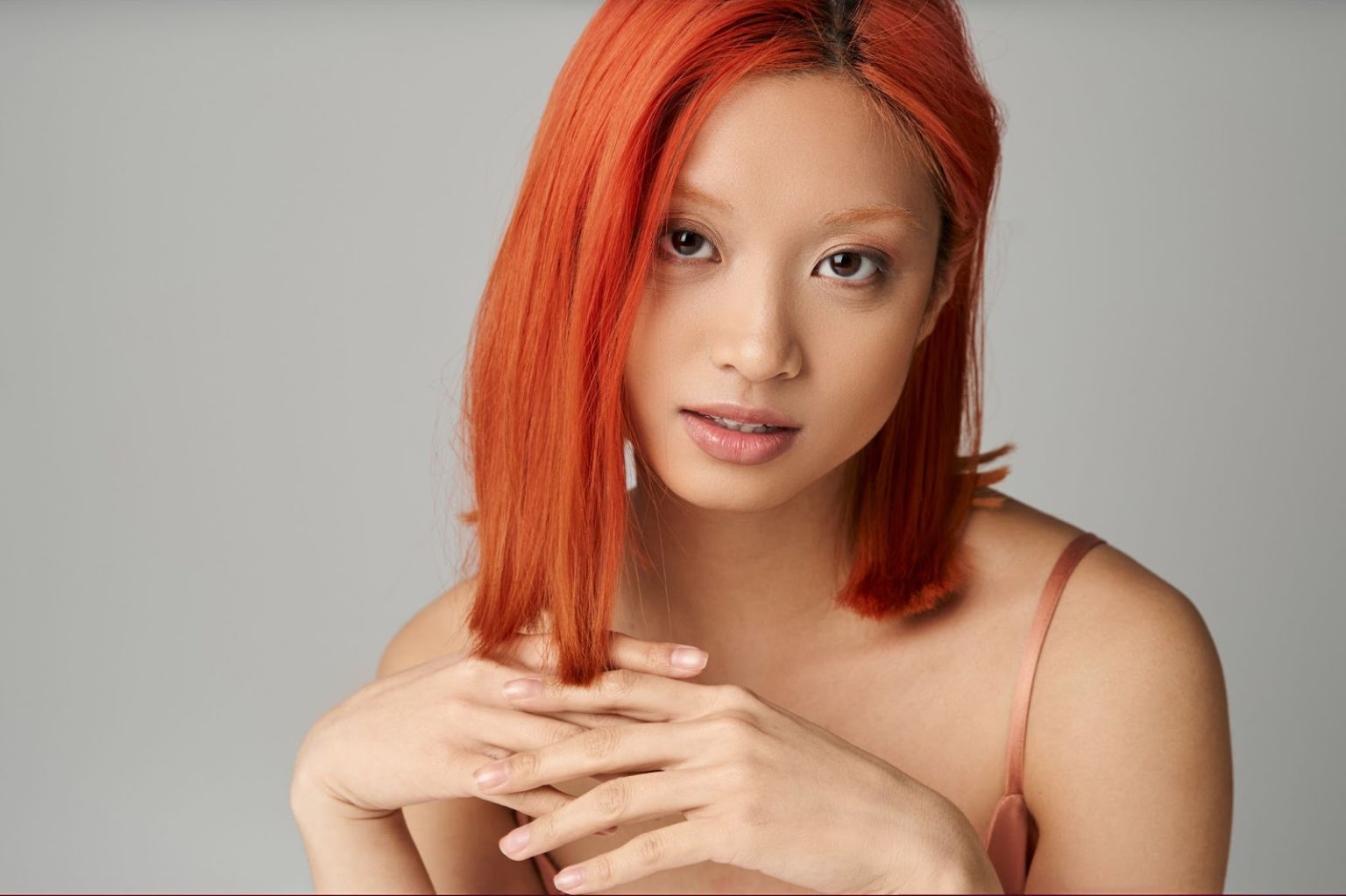 An Asian woman with vibrant red-orange hair color confidently poses for a selfie, showcasing her bold and stylish transformation.